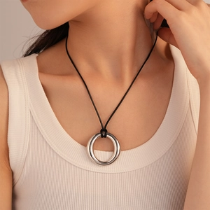 Close-up of minimalist silver ring pendant on a black cord necklace worn by a model