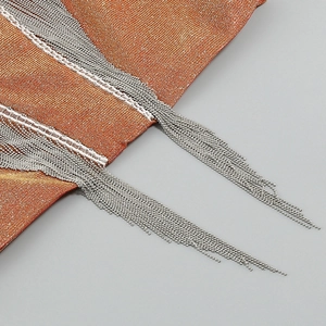 Detail of orange metallic knit fabric with elegant silver beaded chain fringe tassels