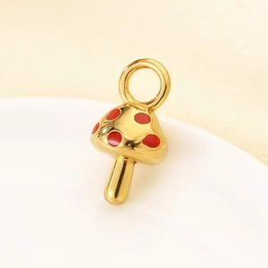 Macro shot of gold stainless steel mushroom pendant with red enamel details on a white dish