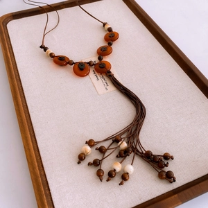 Detail of ethnic style necklace featuring orange resin charms and wooden bead tassels