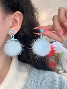 Close-up of light blue fluffy pom-pom earrings with heart-shaped stud on ear