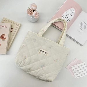 Macro detail of cream quilted tote bag featuring rainbow bow embroidery and branded label