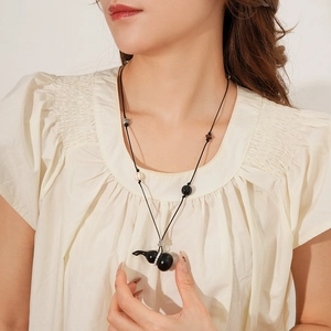Close-up of black gourd pendant with pearls on a wax rope necklace worn by a model