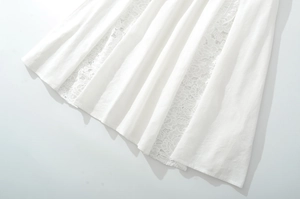 Detailed view of white pleated skirt fabric featuring elegant lace patchwork and texture