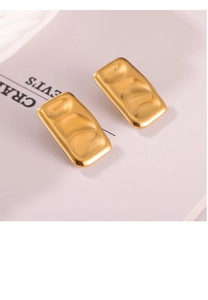 Detailed view of golden rectangular earrings with irregular concave texture on a magazine