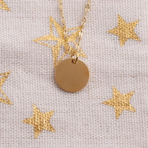 Detailed view of a gold-finish round pendant necklace on a star-patterned fabric