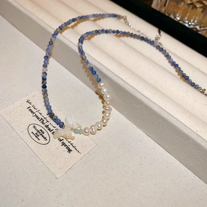Détail du collier avec perles bleues facettées, perles blanches et pendentif papillon