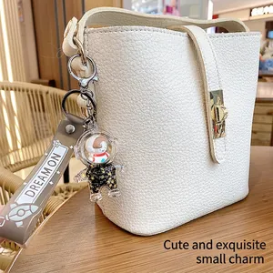 White lychee leather bucket bag with gold lock and astronaut keychain on a wooden table