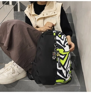 Detail of a black and geometric green backpack with an astronaut pendant and woven strap
