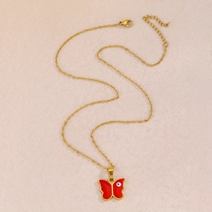 Goldene Edelstahlkette mit rotem Schmetterlings-Evil-Eye-Anhänger auf beigem Hintergrund