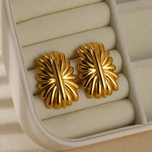 Detailed view of golden flower earrings with radial texture on beige velvet tray