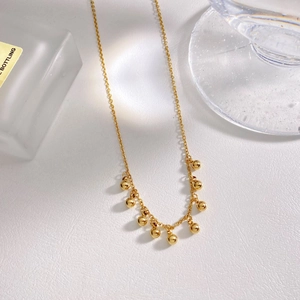 Minimalist gold plated stainless steel necklace with round beads on a textured white surface