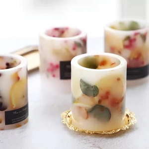 Handmade hollow cylindrical candle mold with dried flowers on a golden decorative tray