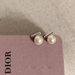Macro detail of elegant pearl stud earrings with silver bars on soft fabric background