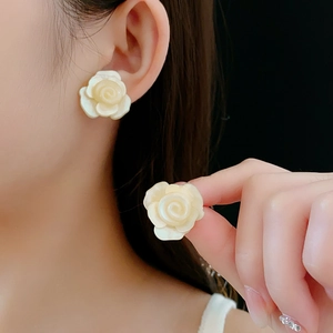 Gros plan de boucles d'oreilles roses en résine crème portées et tenues à la main