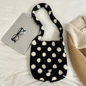 Detail of black plush shoulder bag with white polka dots on a cozy bedding setup