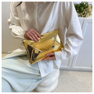 Close-up of golden envelope clutch bag featuring glossy crocodile pattern and metal trim