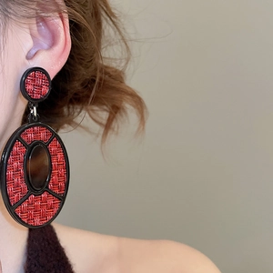 Detail of red woven texture and black oval pendant earring on a female model