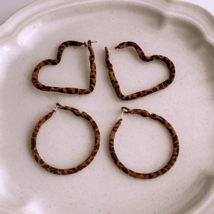 Detail view of heart and round leopard print earrings on a beige ceramic plate