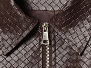 Detail of dark brown woven leather texture with a silver metal zipper on a cropped jacket