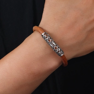 Macro shot of brown leather braided bracelet featuring a hollowed silver metal tube detail