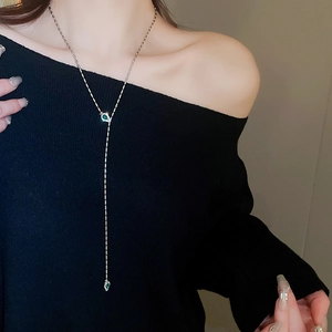 Close-up of golden Y-shaped tassel necklace with elegant green teardrop gemstones