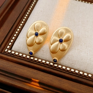 Macro shot of vintage gold teardrop earrings with floral relief and blue gemstones