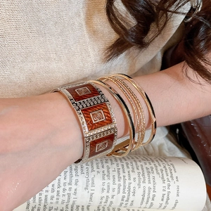 Close-up of a stacked bracelet set featuring red-brown enamel squares and gold-tone rings