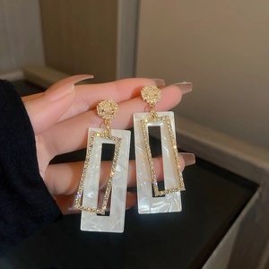 Macro shot of gold geometric earrings with white marble inlay and sparkling rhinestones