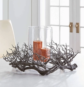 Detail of black twig-style candle holder with glass shade and orange pillar candles