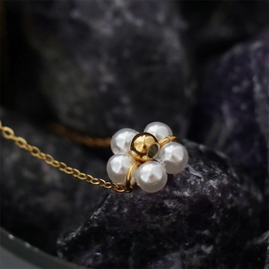 Macro view of a 18K gold-plated floral pendant with white pearls on a dark stone background