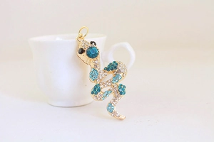 Detail of a gold snake keychain pendant with blue and white crystals on white surface