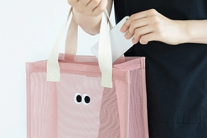 Pink mesh beach bag detail showing a person placing a smartphone inside for storage