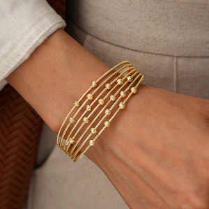 Close-up of gold layered bangles featuring spiral textures and faceted beads on wrist