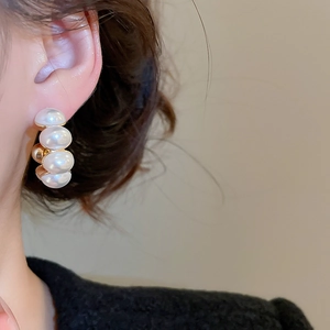 Close-up of elegant C-shaped gold-plated pearl earrings worn by a model in French style