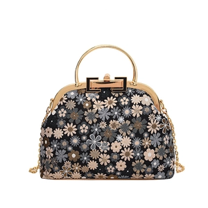 Close-up of vintage floral embroidery and metal ring handle on a shell-shaped bag