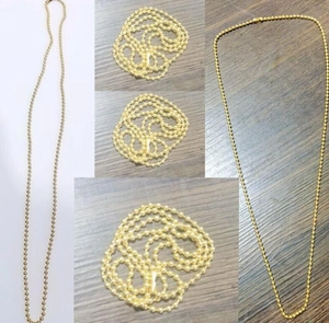 Dettaglio della collana a catena a sfere dorate in acciaio su fondo di legno rustico