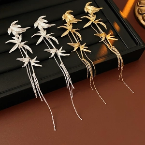 Detail of silver and gold bamboo leaf tassel earrings on a black jewelry display