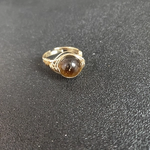Detailed macro view of handmade gold wire-wrapped ring with a round brown natural gemstone