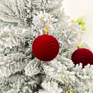 Gros plan de boules de Noël en velours rouge texturé sur une branche enneigée