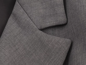 Détail macro du revers d'un tailleur gris montrant la texture fine du tissu et les coutures