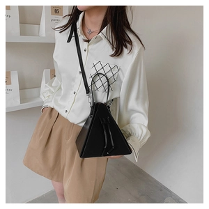 Fashionable black triangular handbag with ring handle and adjustable strap on a model
