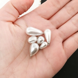 Close-up of white teardrop imitation pearl pendants in various sizes held for scale