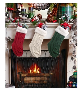 Three knit Christmas stockings in red white and green hanging by a warm fireplace