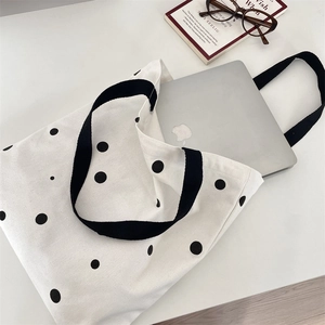 Spacious white canvas tote bag with black polka dots shown holding a laptop
