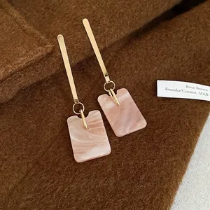 Elegant gold earrings with square marble pattern pendant on brown fabric background