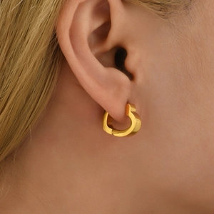 Close-up of a gold heart-shaped huggie earring on ear showing polished metal texture