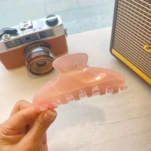 Vue détaillée d'une grande pince à cheveux en acétate nacré rose-orange à la main