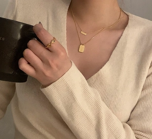 Detail of layered gold pendant necklaces and twisted ring on model with coffee cup