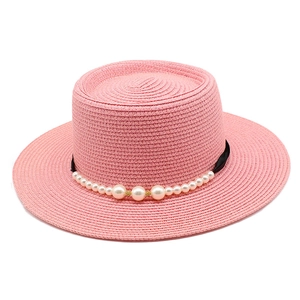 Dettaglio di un cappello di paglia rosa con nastro nero ed eleganti decori di perle